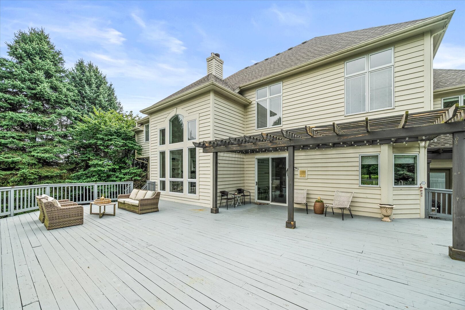 Rear of a beige home with a spacious deck, outdoor seating, and a wood pergola.