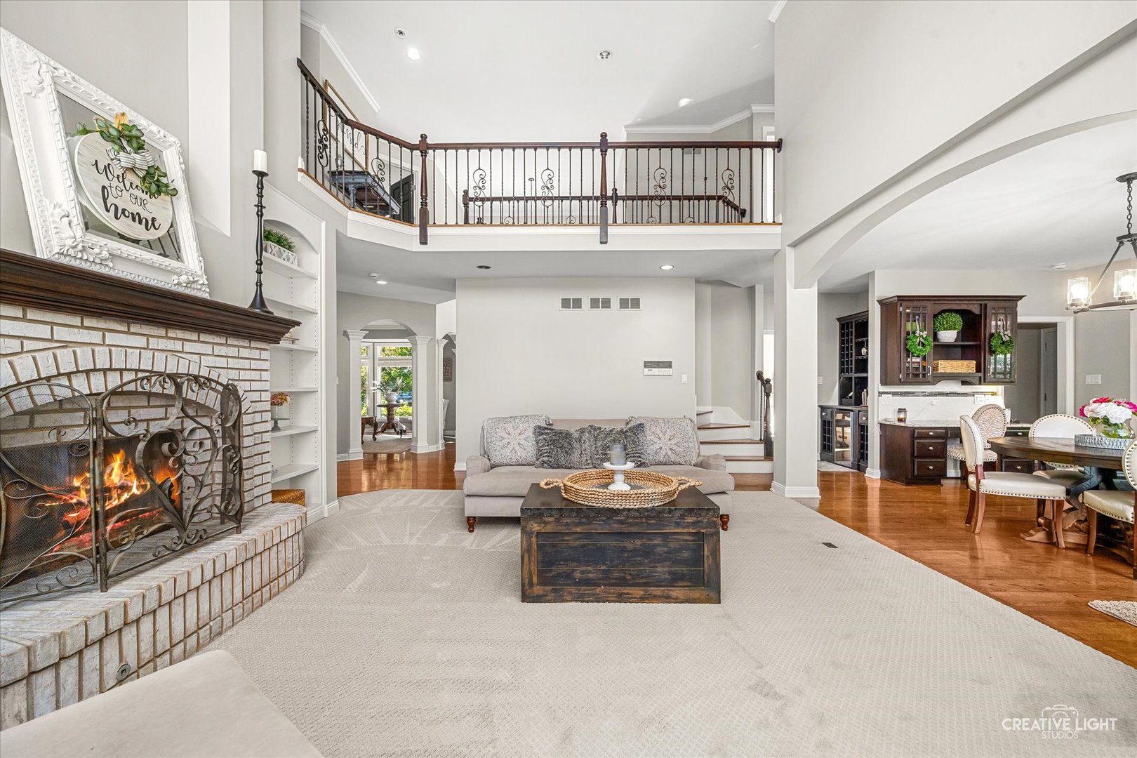 Two-story living room with a brick fireplace, gallery railing, and adjoining dining area.