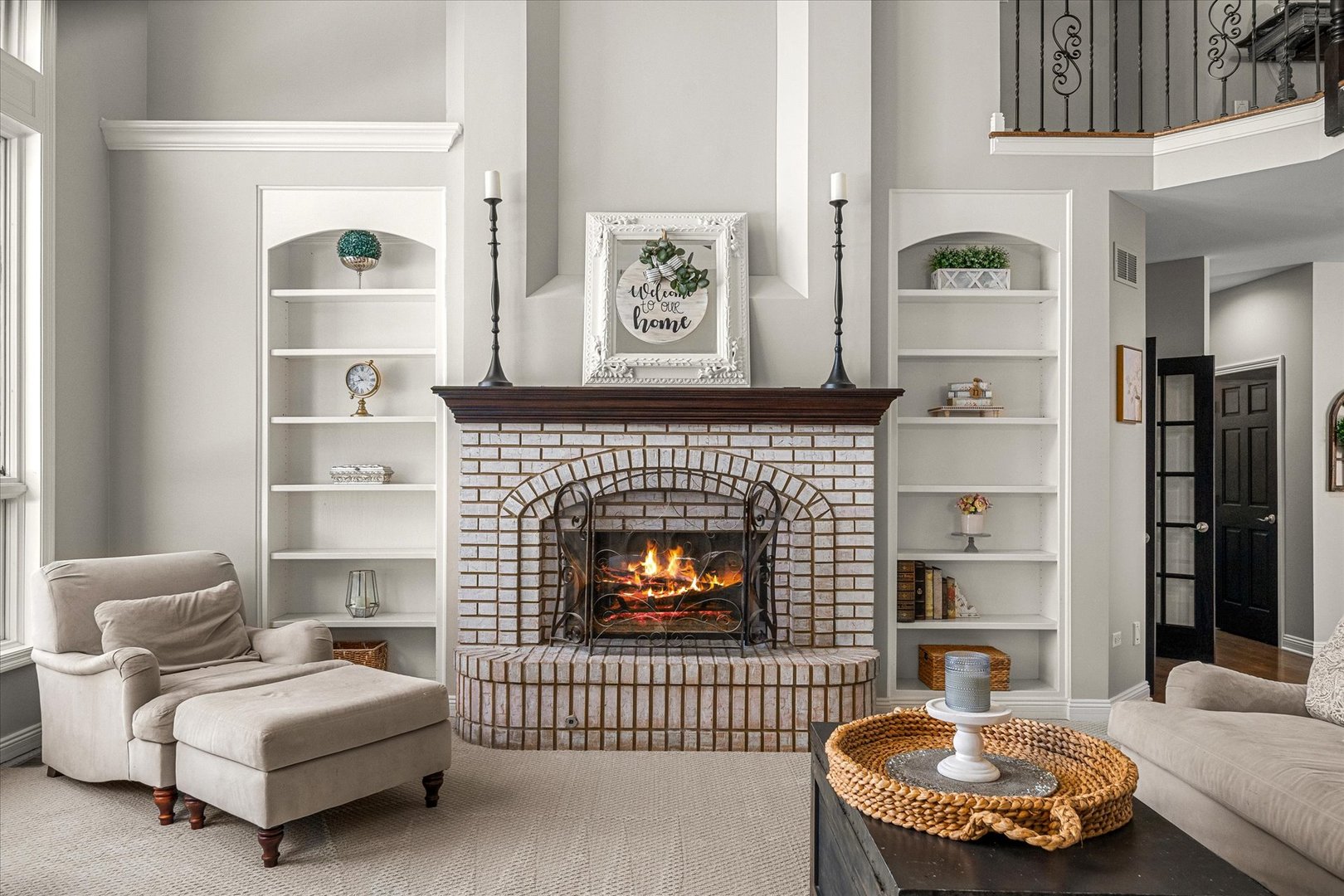 Living room with a lit white-brick fireplace, built-in shelves, and a view of the upper-level railing.