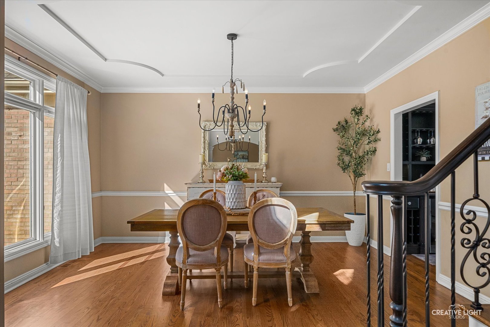 Dining room with a wood table, upholstered chairs, chandelier, ornate mirror, and hardwood floors.
