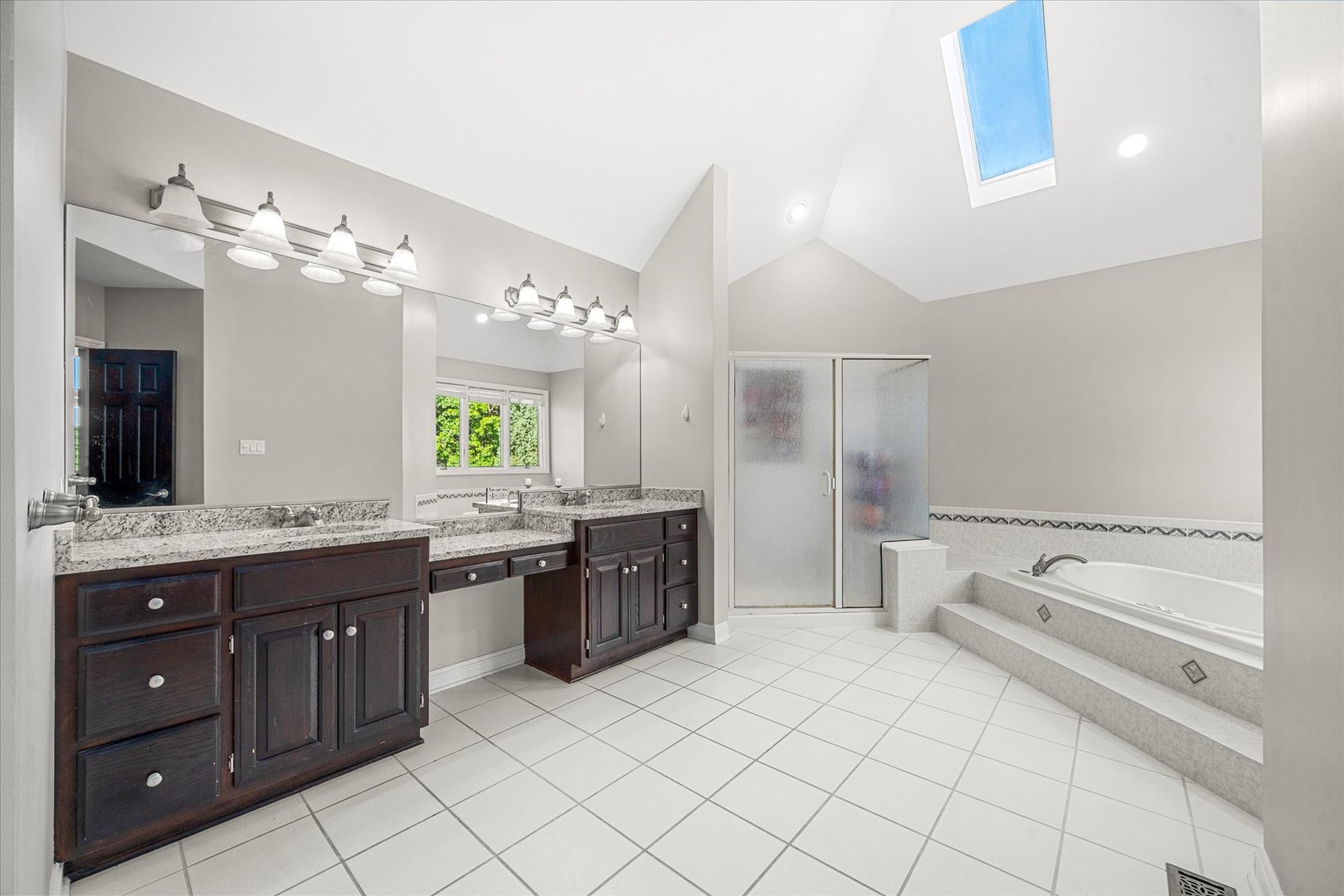 Primary bathroom with a dark double vanity, granite counters, raised soaking tub, and skylight.