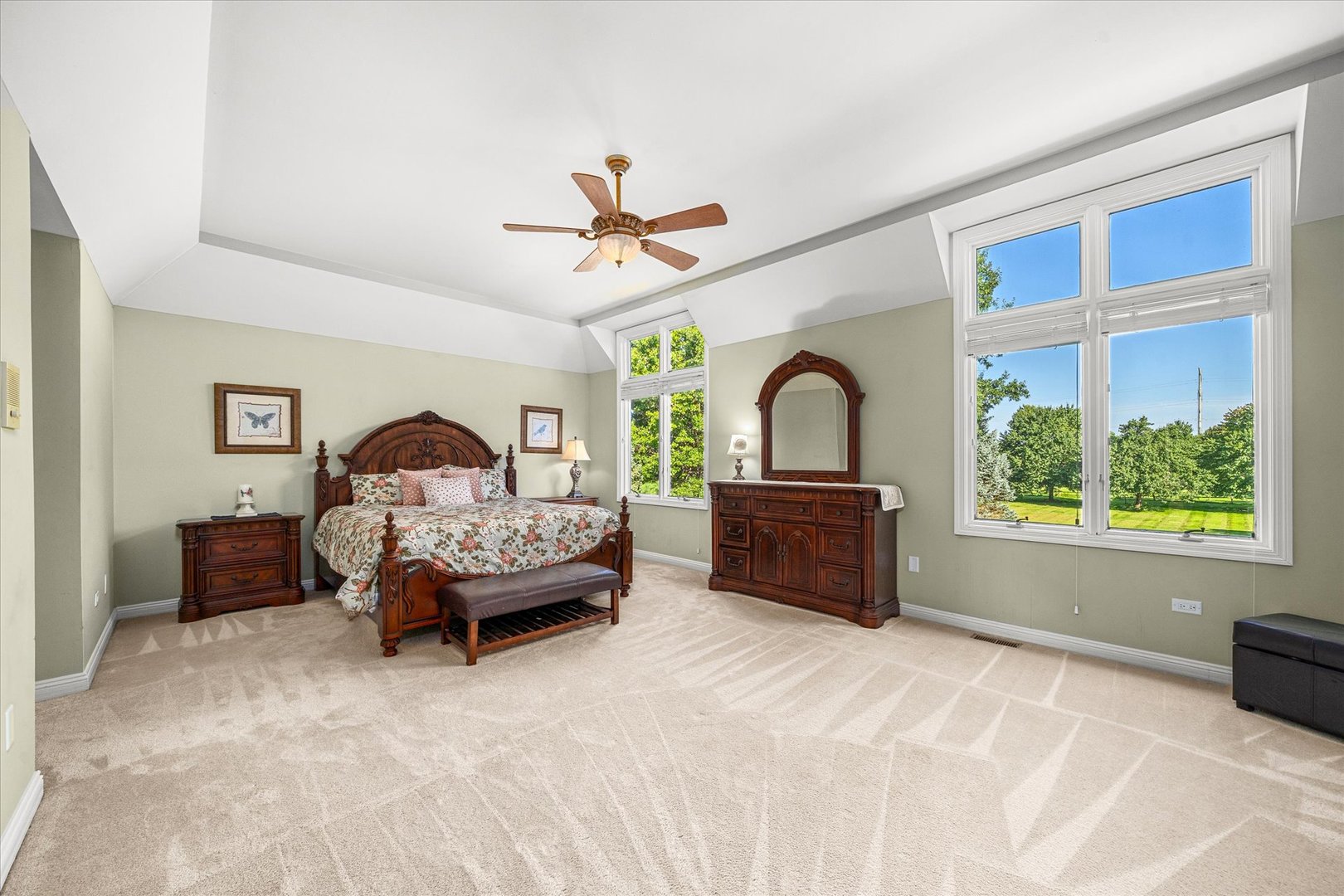 Furnished bedroom with dark wood furniture, a high angled ceiling, and tall windows overlooking a green lawn.
