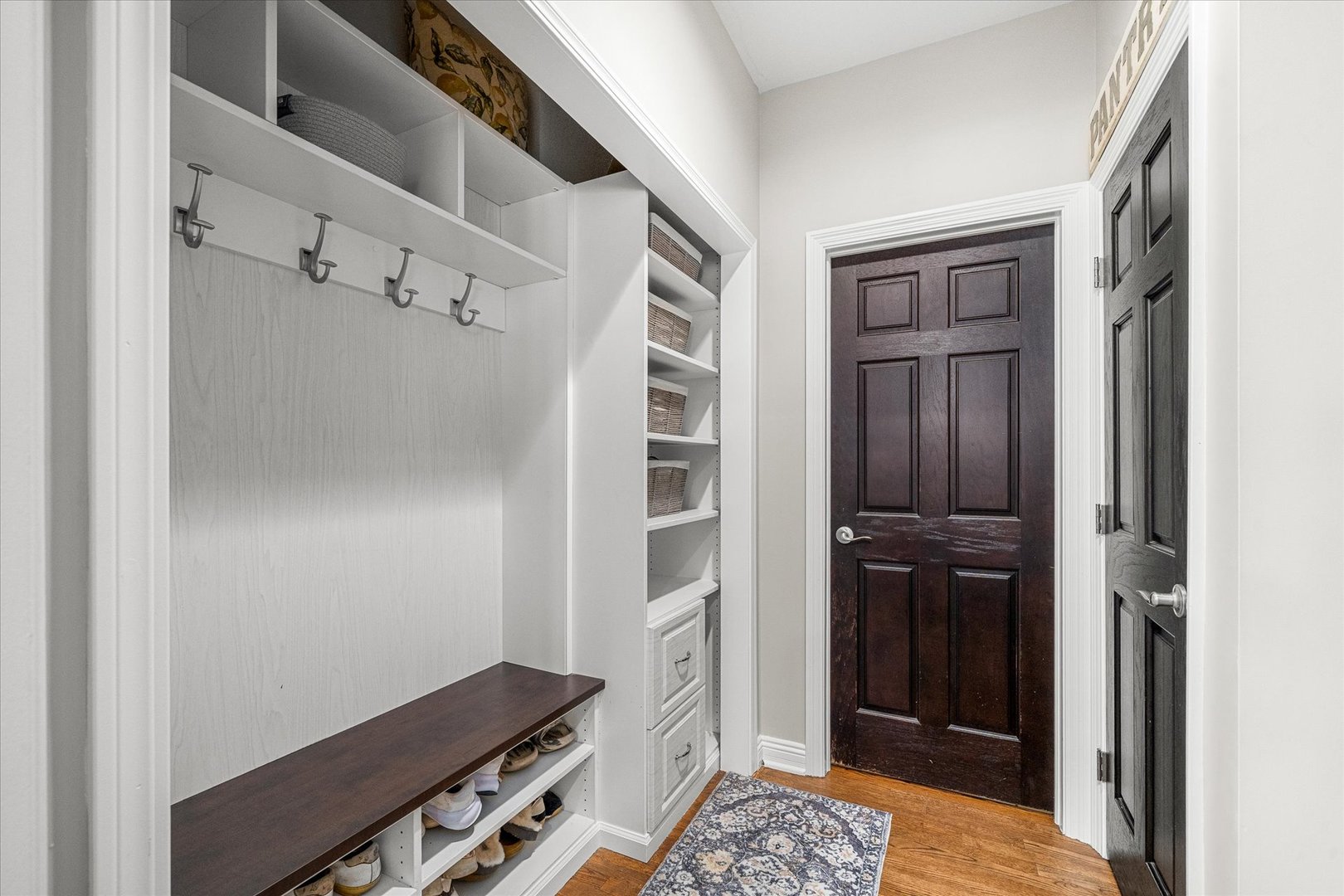 Entryway with built-in mudroom storage, coat hooks, a dark bench, shoe cubbies, and paneled doors.
