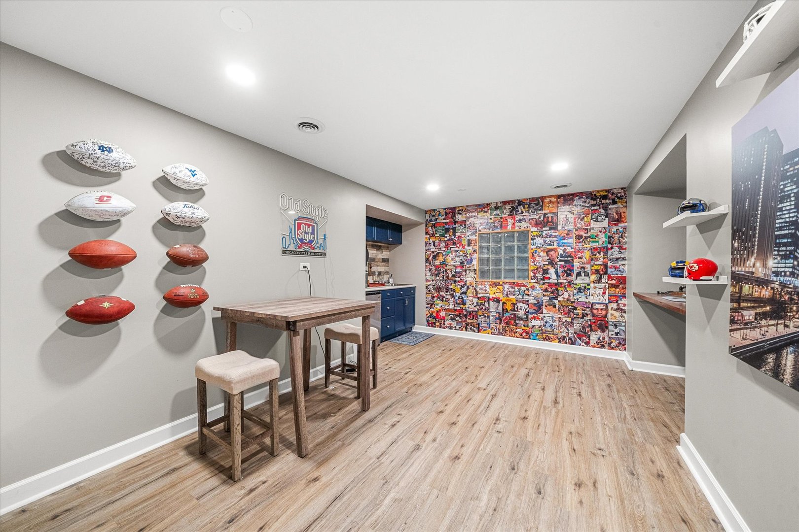 Sports-themed room with wall-mounted footballs, a sports magazine collage, and a small bar kitchenette.