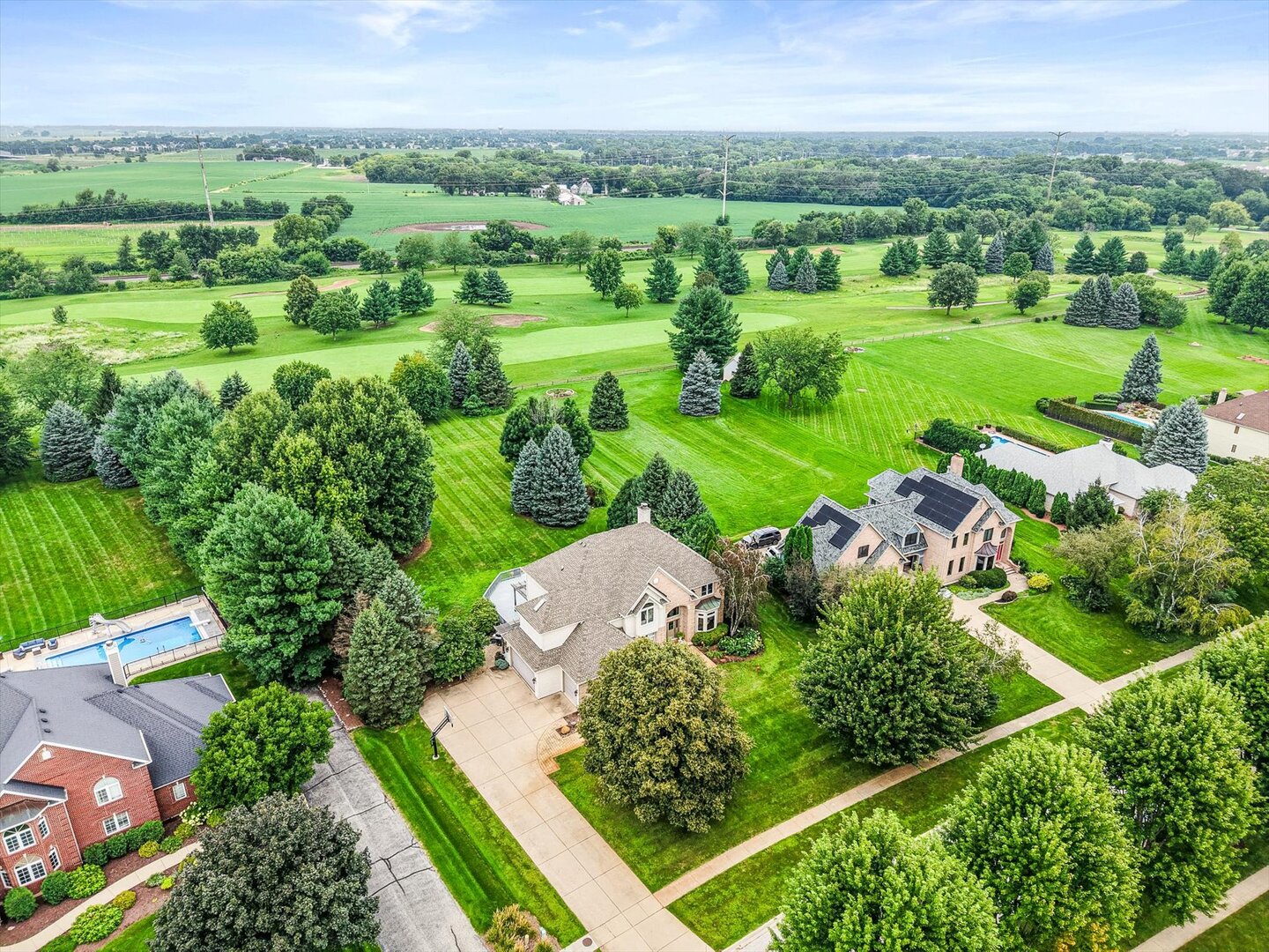Aerial view of homes beside manicured golf course greens, with mature trees and a swimming pool.