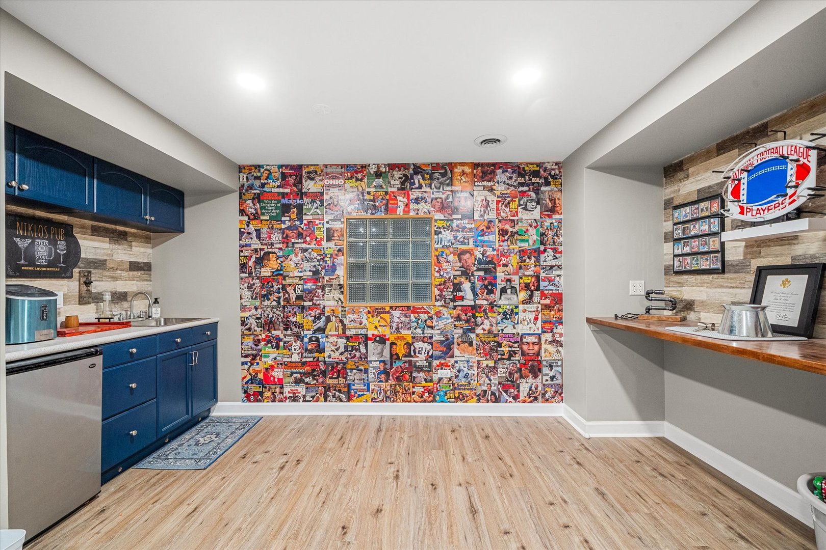 Finished basement entertainment room with a blue wet bar and sports magazine collage wall.