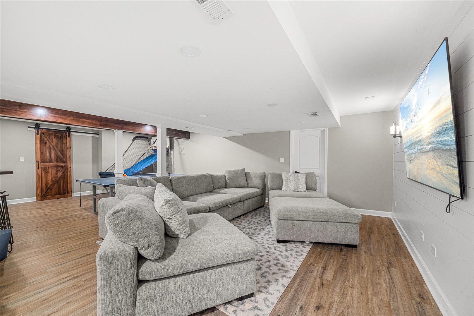 Basement recreation room with a gray sectional, ping-pong table, and sports practice net.