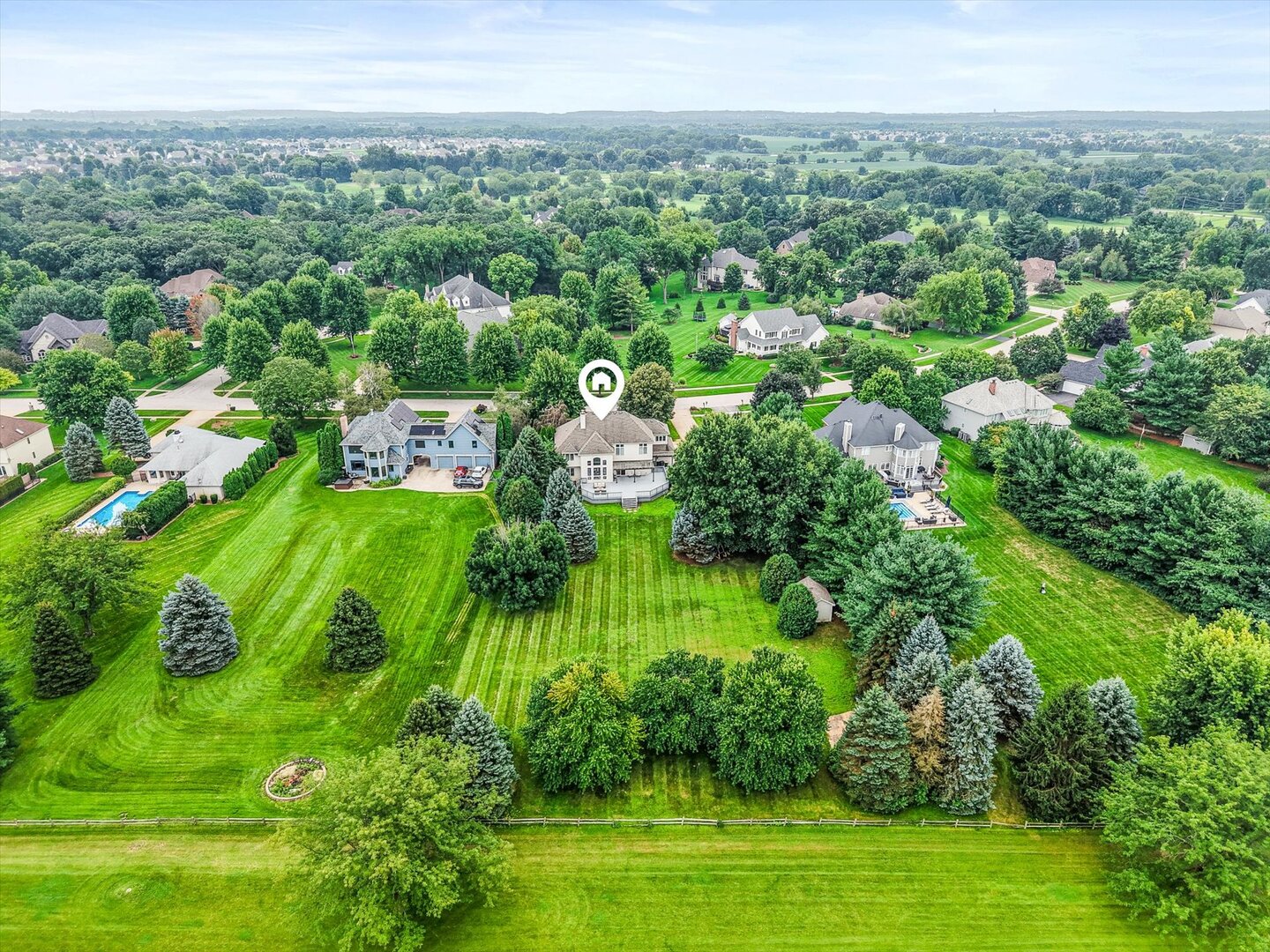 Aerial view of a home amid mature trees, an expansive striped lawn, and neighboring houses.