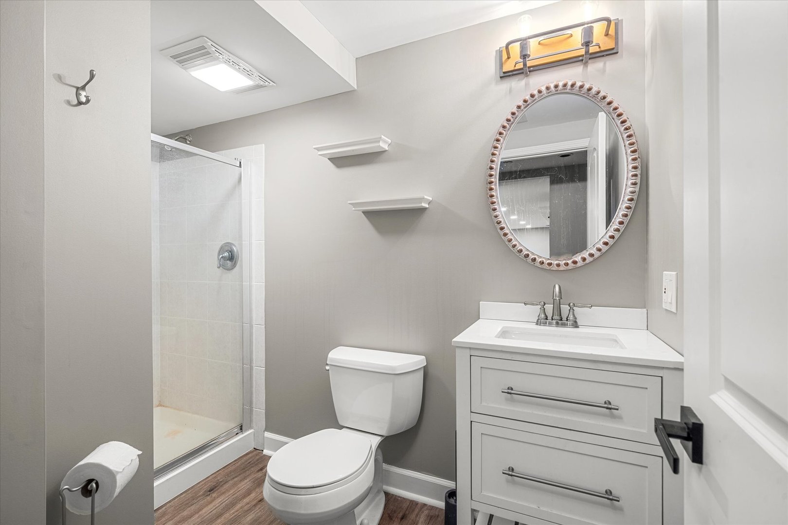 Bathroom with a glass shower, white vanity, and oval framed mirror.