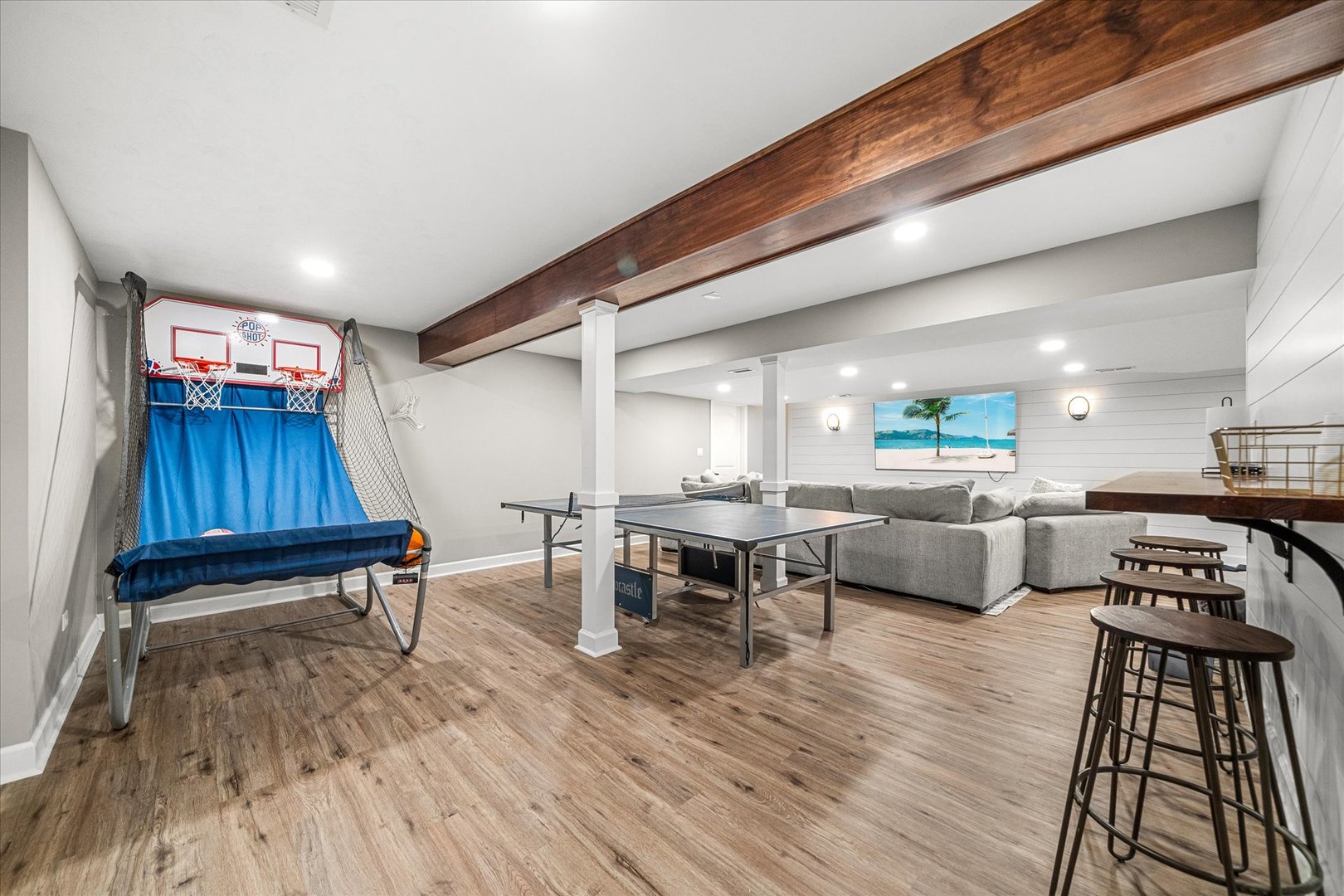 Finished basement game room with ping-pong table, basketball game, sectional sofa, and bar seating.