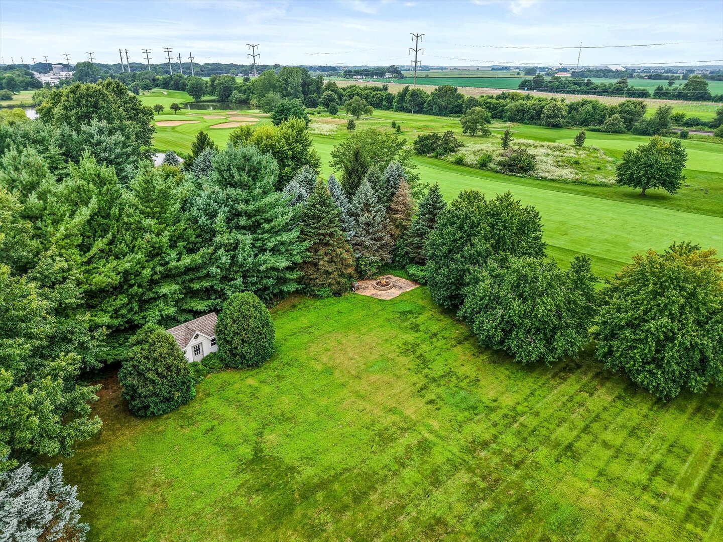 Tree-lined backyard with a fire pit and outbuilding beside a golf course.