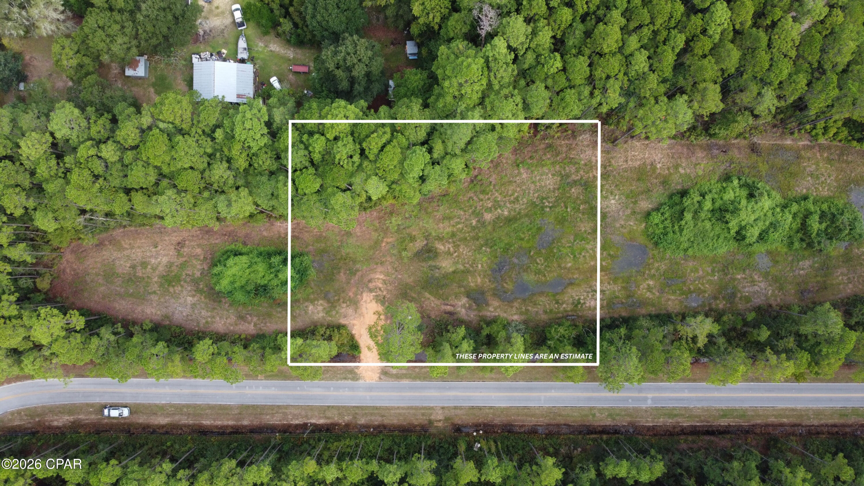 Aerial view of a wooded lot outlined beside a road, with a broad clearing and wet patches.