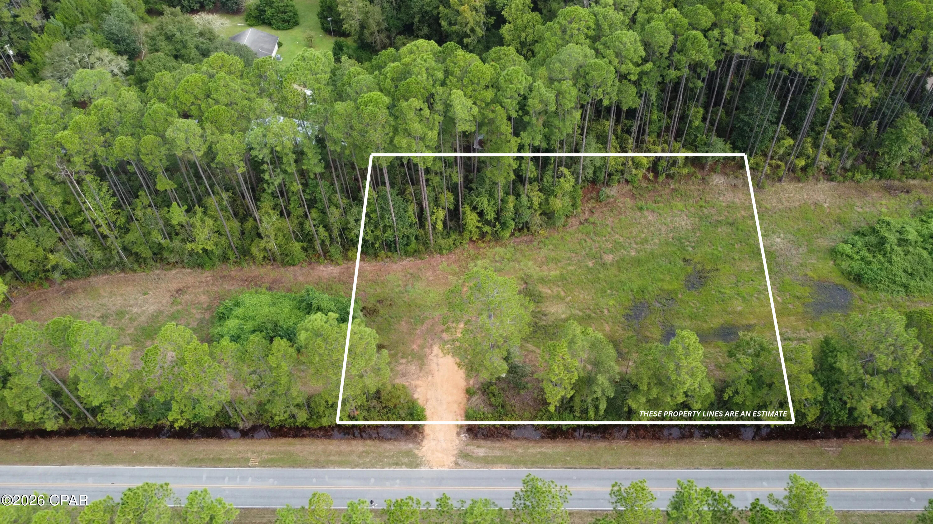 Aerial view of a wooded vacant lot outlined beside a paved road.