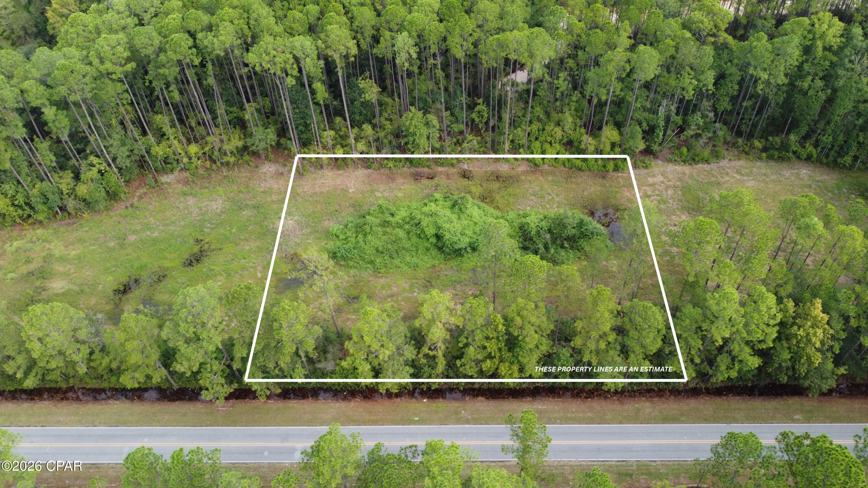 Aerial view of a wooded parcel outlined beside a road, with estimated property boundaries.