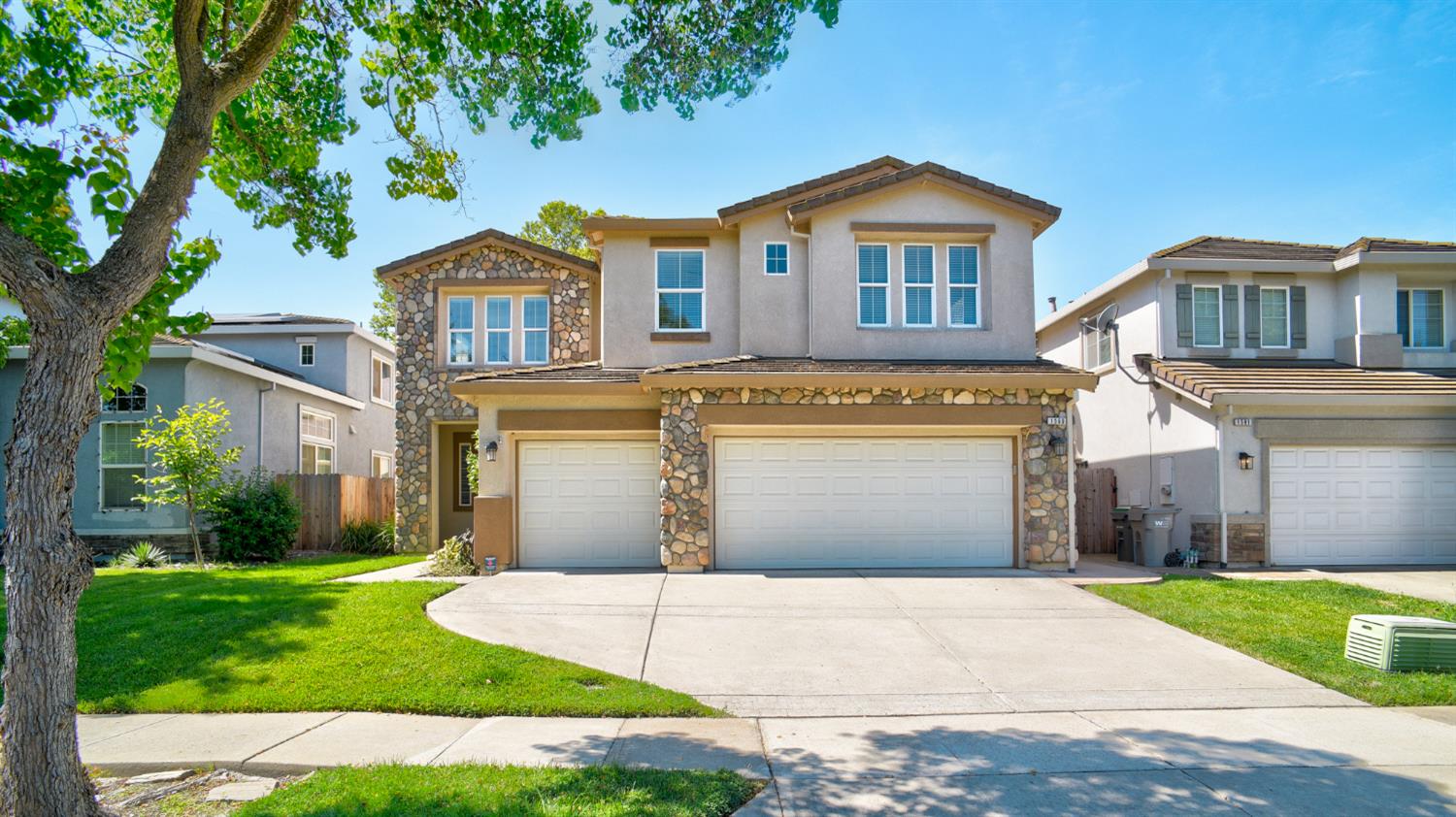 Two-story home with stone accents, attached garages, a front lawn, and a broad driveway.