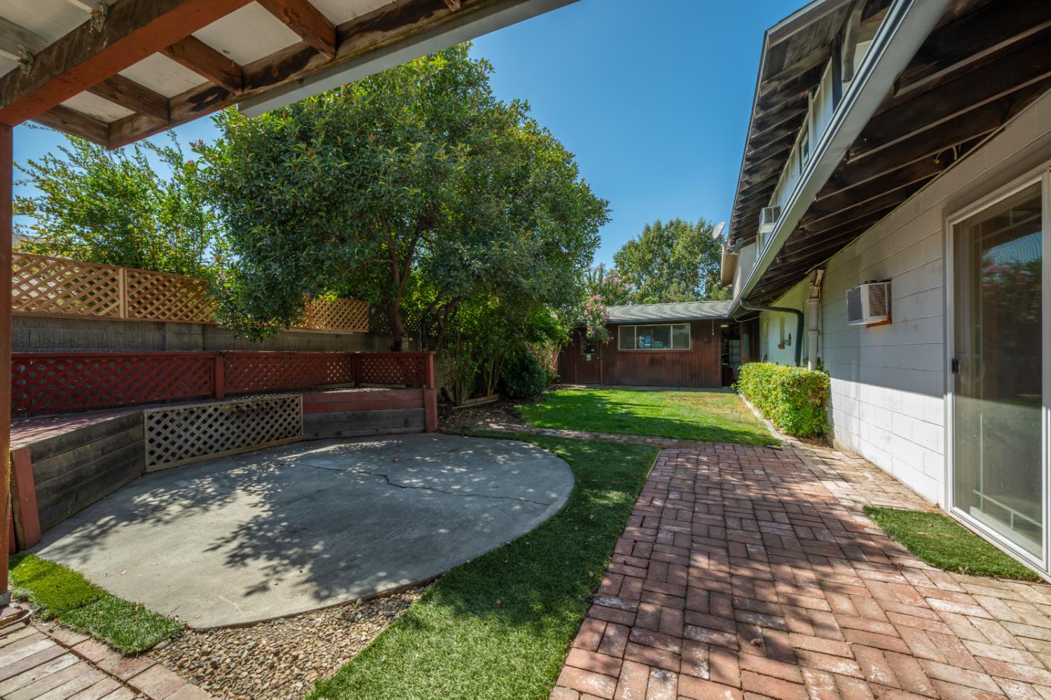 Backyard patio with brick pavers, a circular concrete area, lawn, and mature trees.