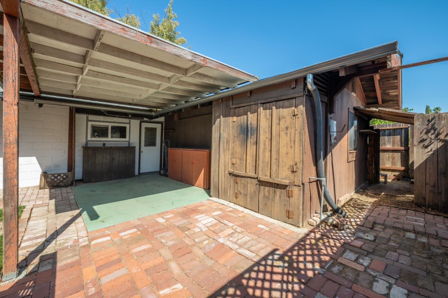 Brick-paved backyard patio with a covered area and weathered wooden outbuildings.