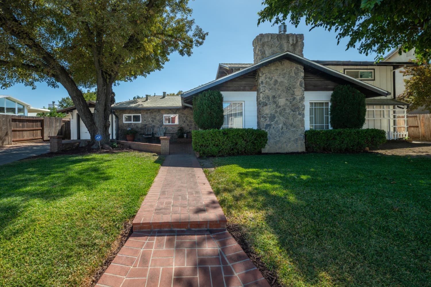 House with a prominent stone chimney, brick walkway, and mature shade trees.