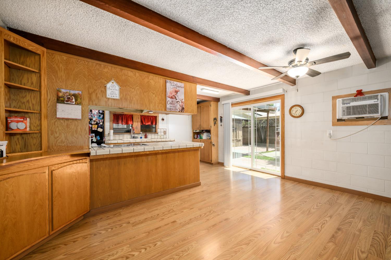 Kitchen with oak cabinetry, tiled peninsula, exposed ceiling beams, and sliding glass doors.