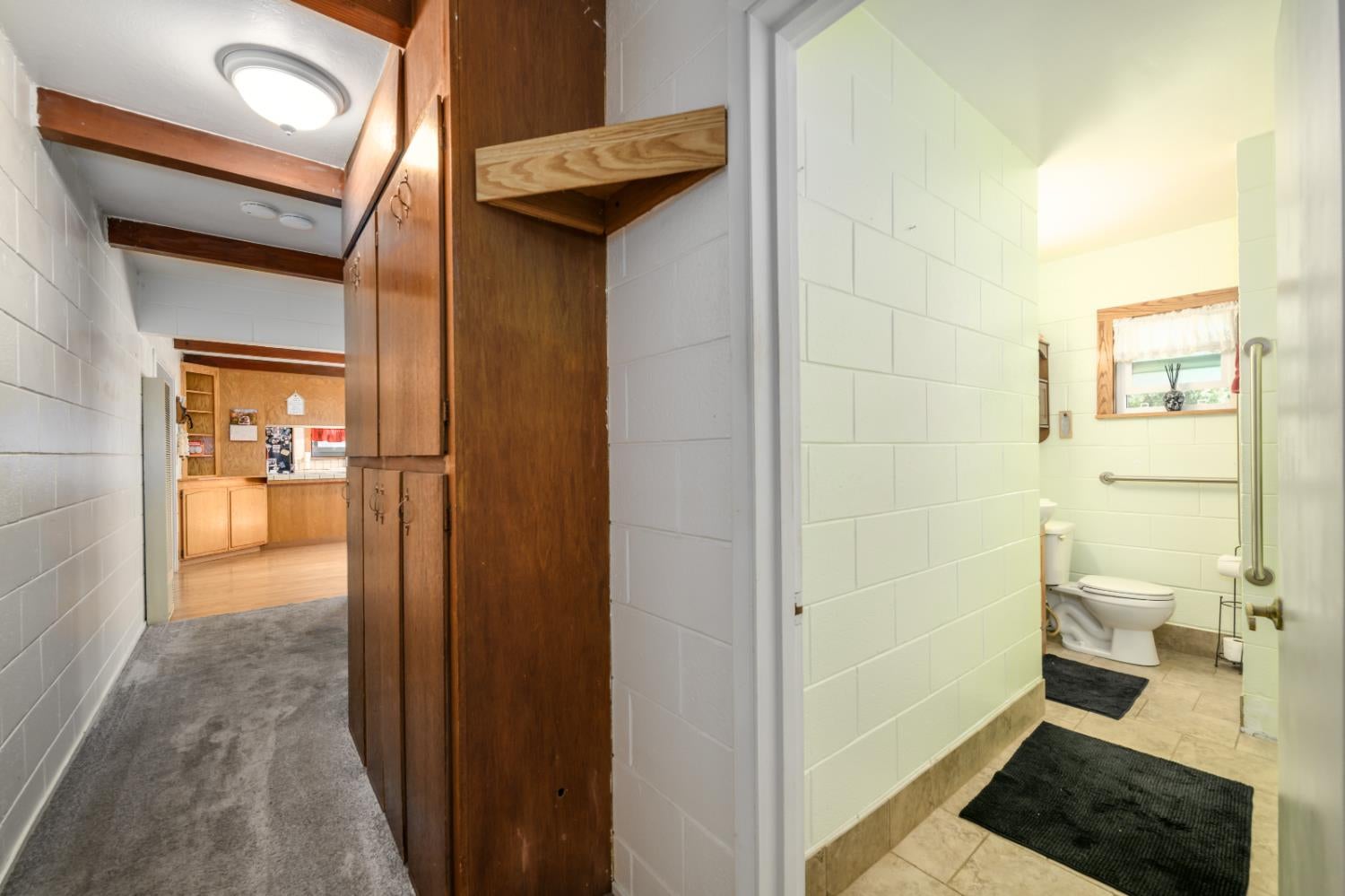 Hallway with dark wood built-ins leading to a tiled bathroom with grab bars and a small window.