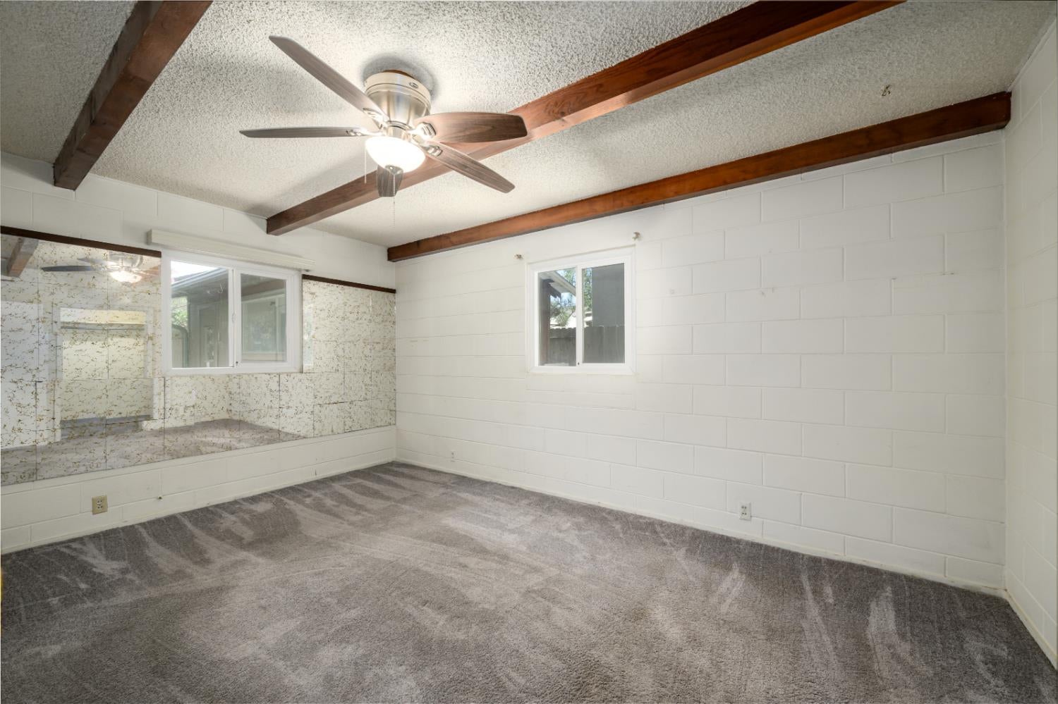Empty carpeted room with exposed wood ceiling beams and a ceiling fan.