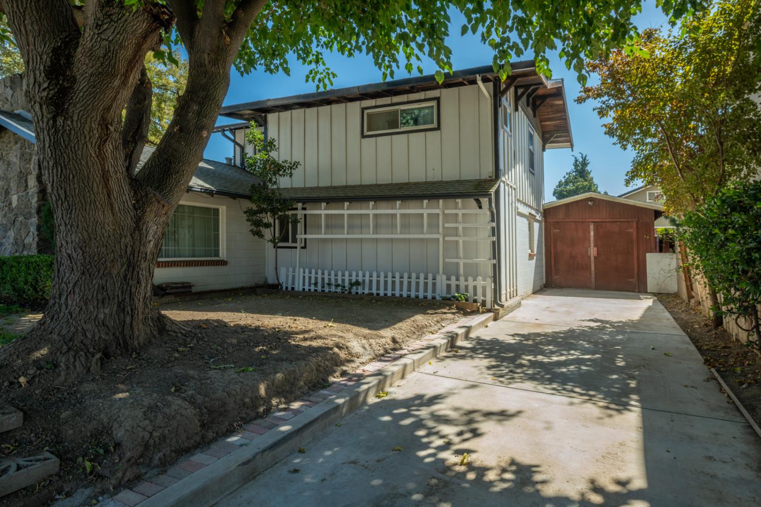 Two-story white home beside a concrete driveway leading to a detached garage, shaded by a large tree.