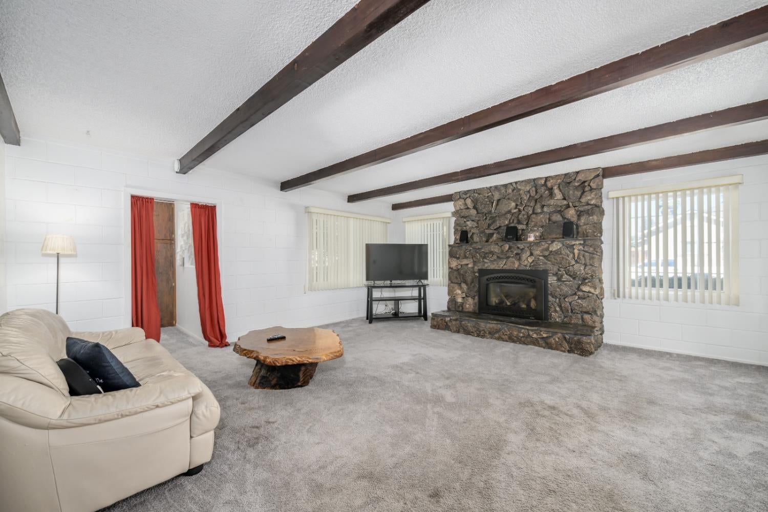 Living room with a stone fireplace and exposed ceiling beams.