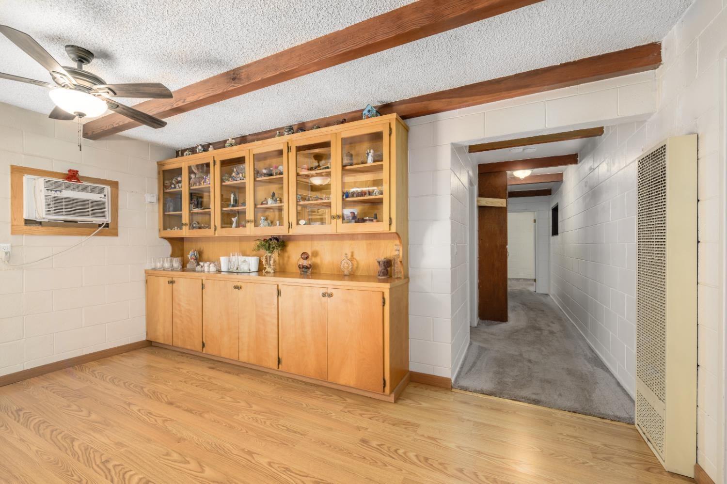 Interior room with a built-in wooden display cabinet, exposed ceiling beams, and a carpeted hallway.