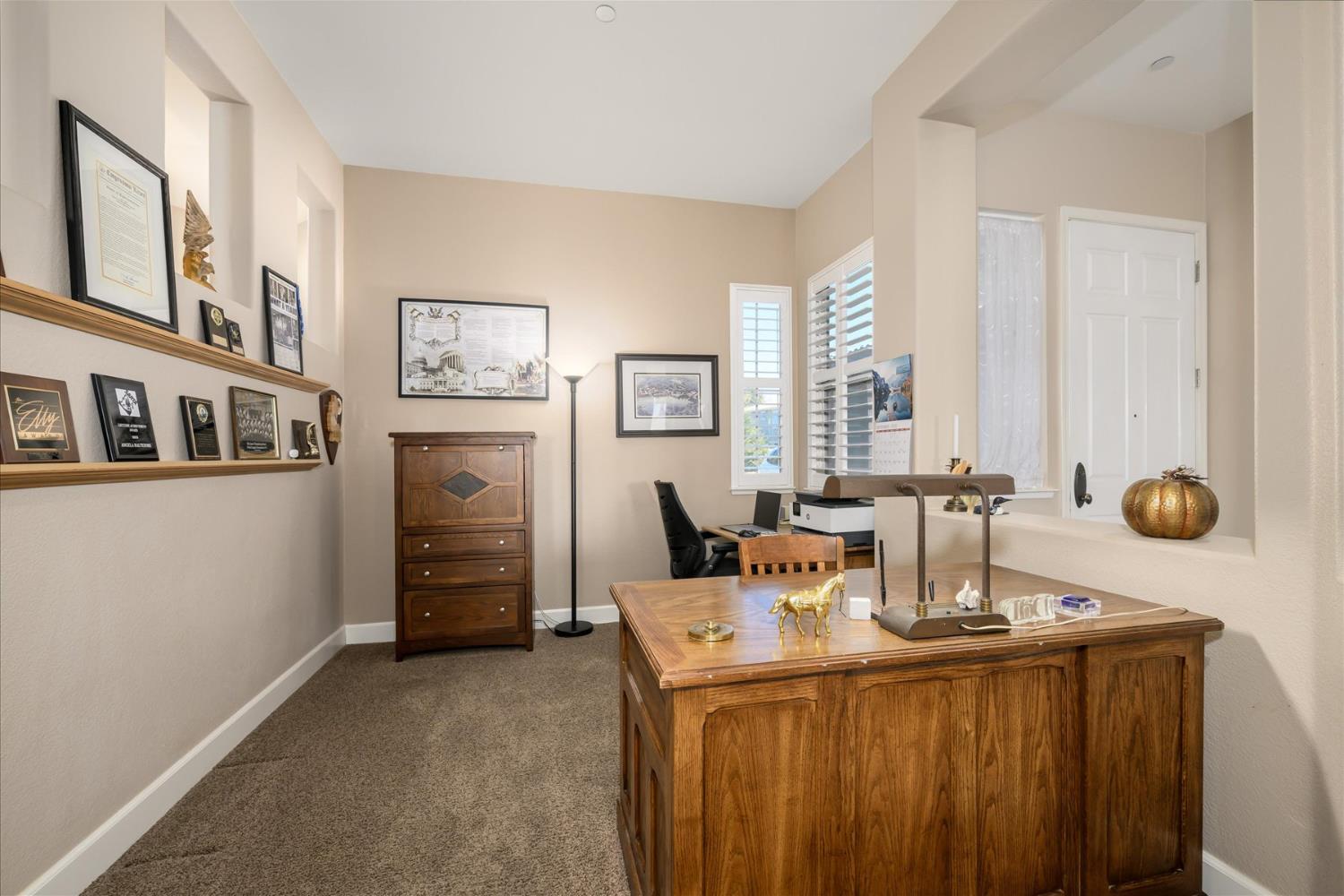 Furnished home office with a large wooden desk and shelves displaying awards.
