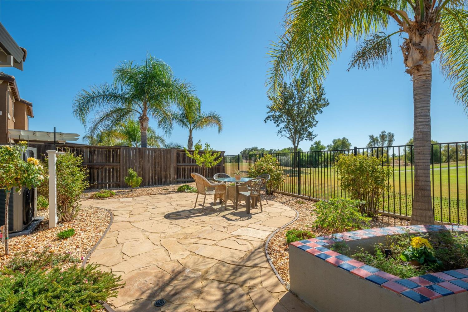 Stone patio with outdoor seating, palm trees, and a golf course beyond the fence.