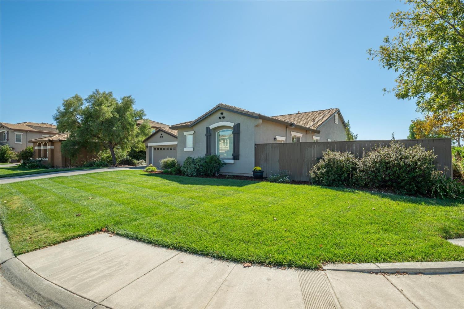 Single-story stucco home with an attached garage, broad green lawn, and dark privacy fence.