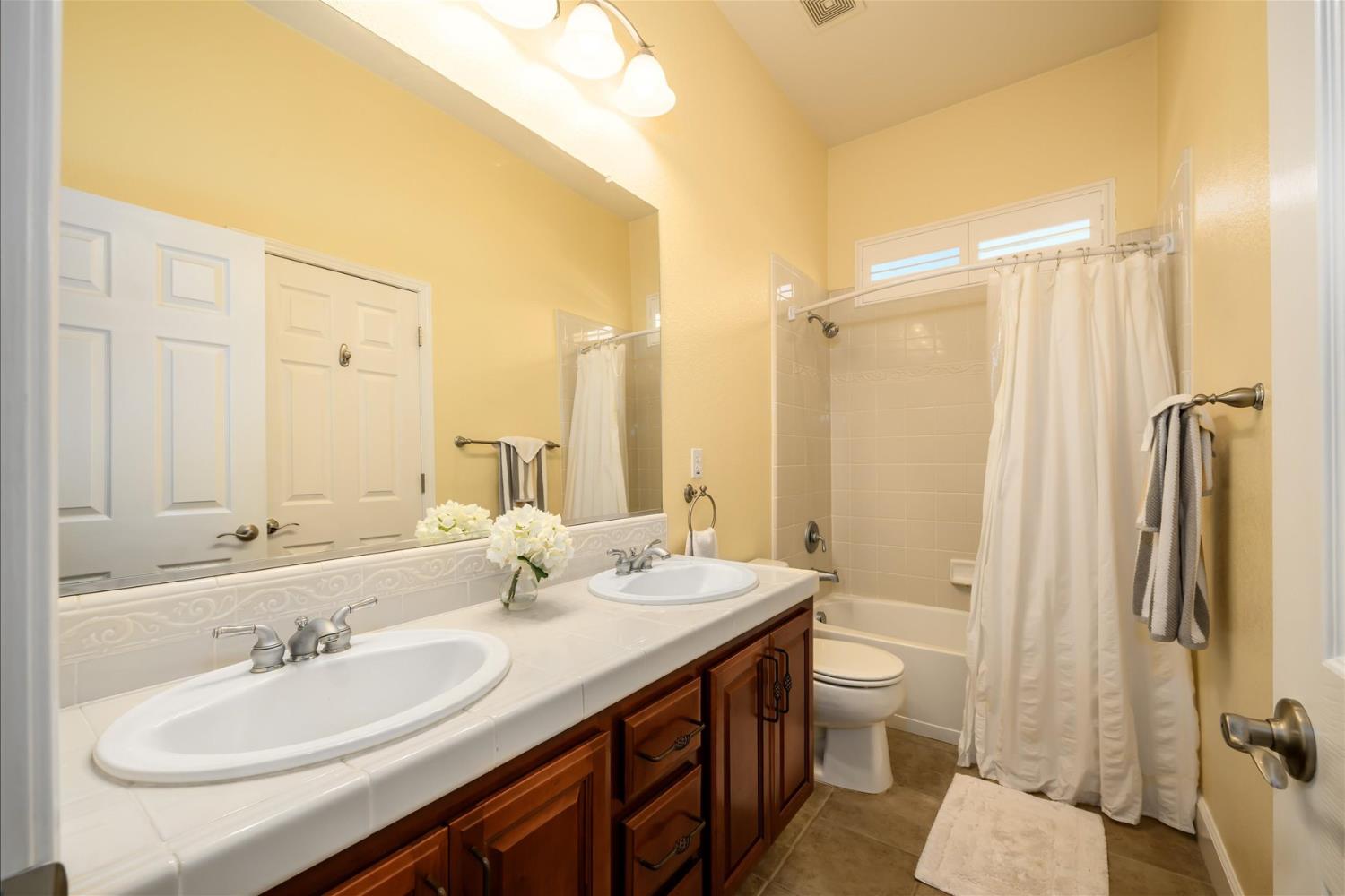 Bathroom with a double-sink vanity, dark wood cabinets, and a curtained tub and shower.