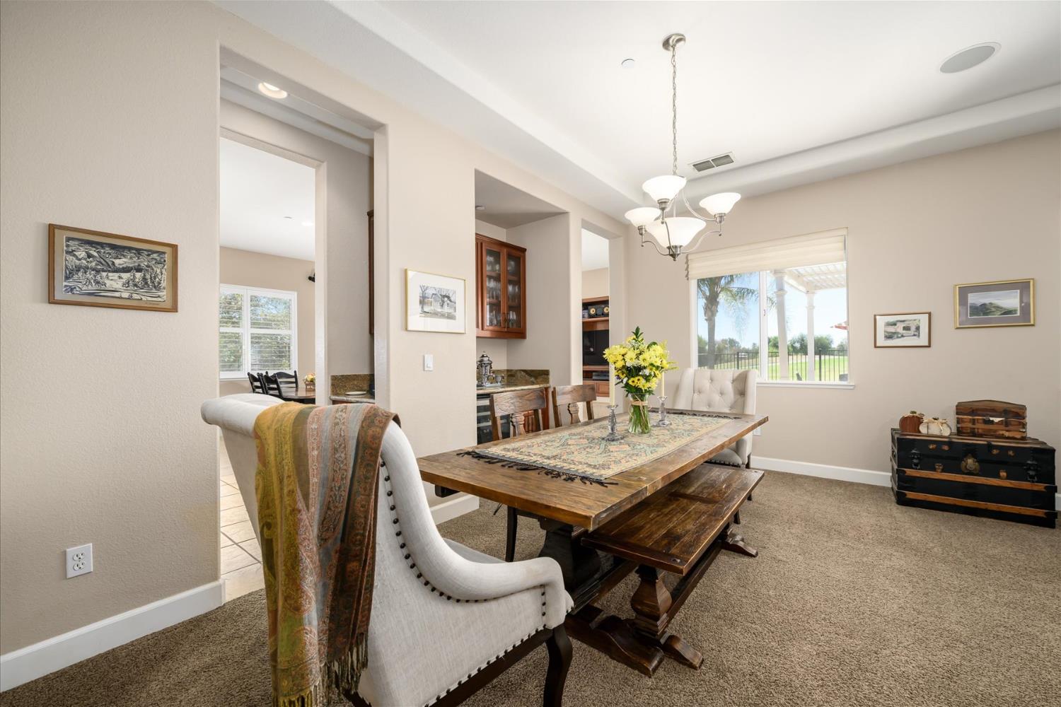 Dining room with a rustic wood table, upholstered chairs, chandelier, and a large window overlooking the yard.
