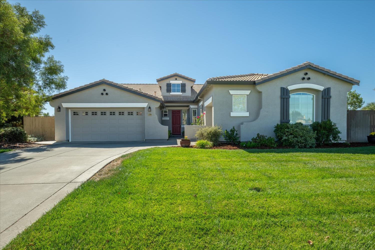 Single-story stucco home with a red front door, two-car garage, and broad green lawn.