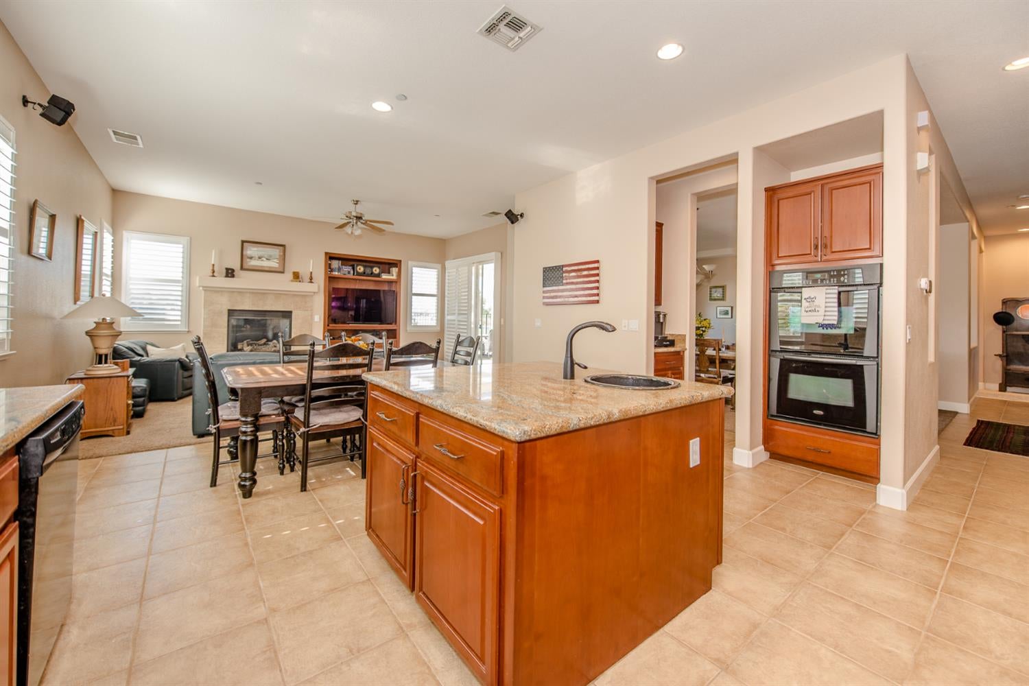 Open-plan kitchen with a granite island, wood cabinetry, and dining and living areas beyond.