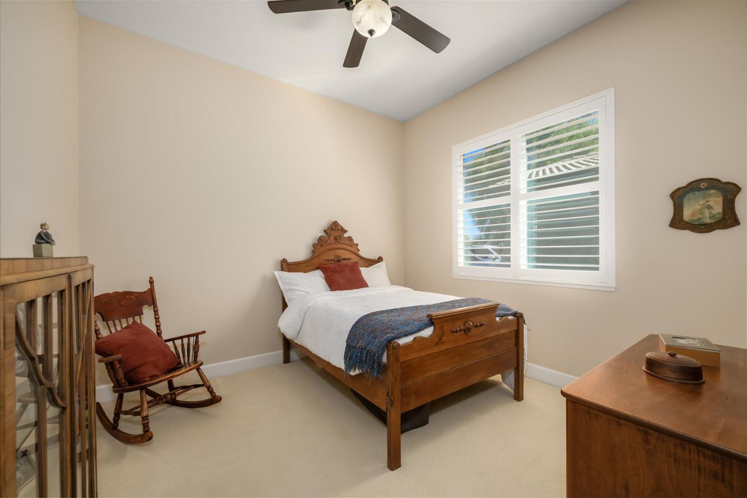 Bedroom with carved wooden bed, rocking chair, and bright shuttered window.