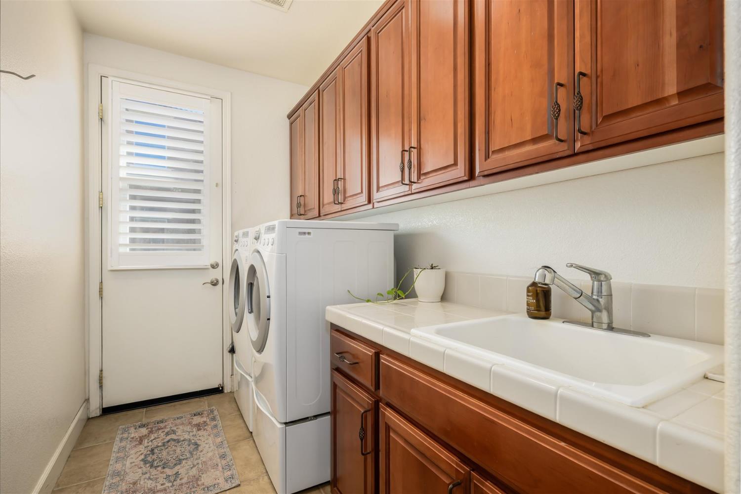Laundry room with wood cabinets, a utility sink, and stacked washer and dryer.