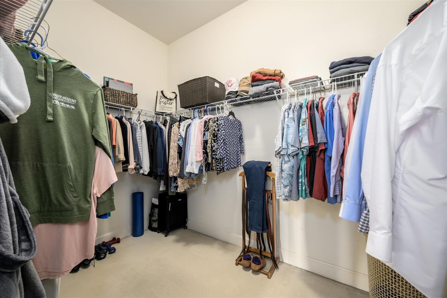 Walk-in closet with clothes lining three walls and folded garments on overhead shelves.