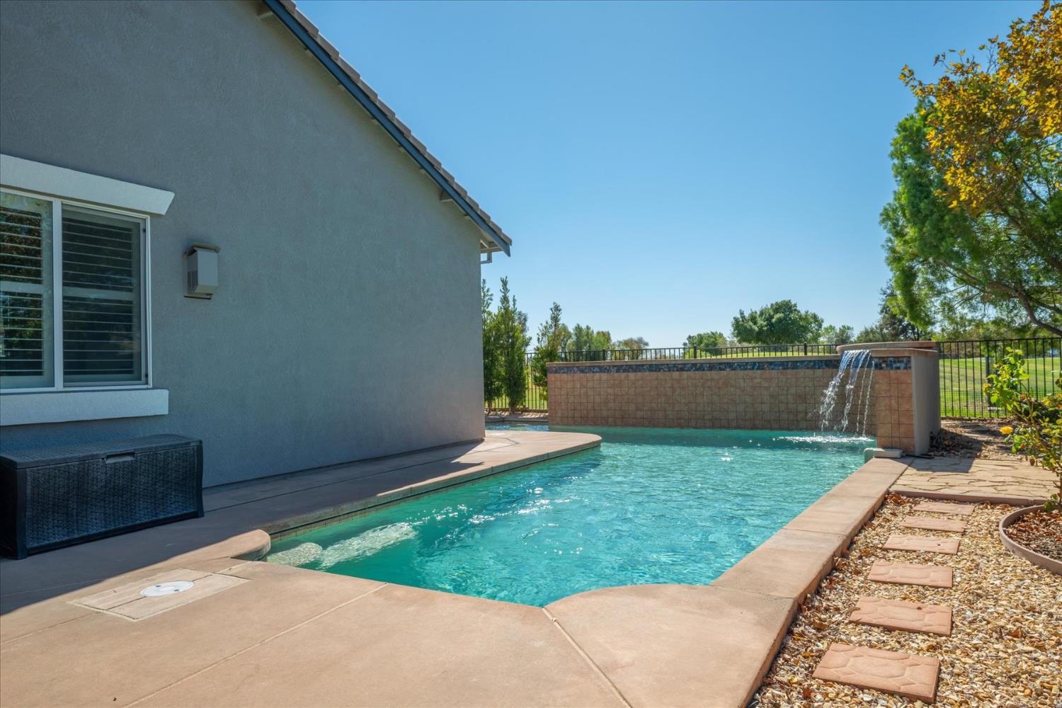 Backyard pool with a raised waterfall wall, concrete deck, and stepping-stone path.