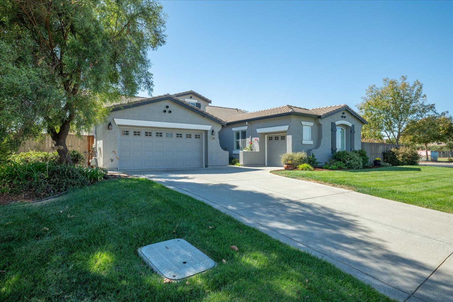 Gray stucco home with two garage doors, a curved driveway, and a landscaped front lawn.