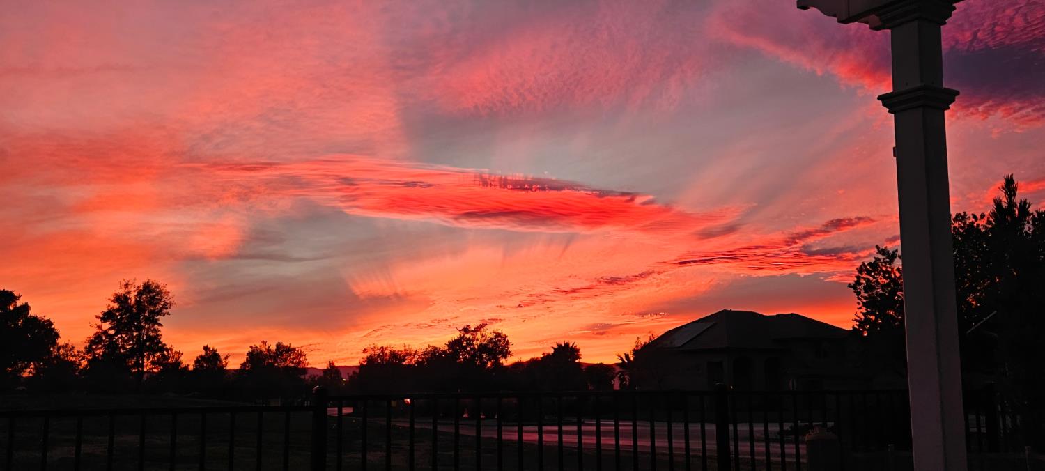 Fenced backyard and covered patio silhouetted against a vivid red-orange sunset.