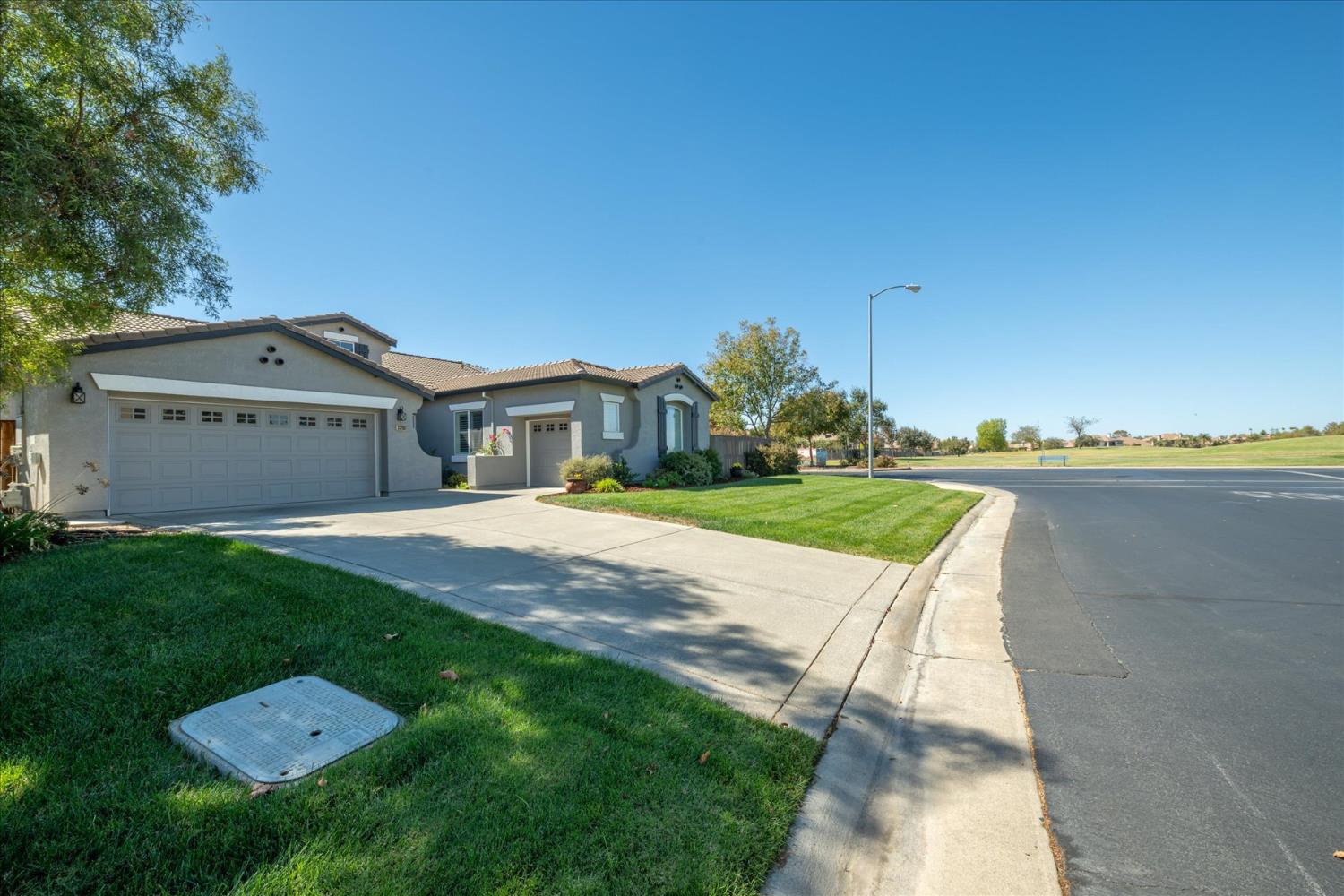 Gray stucco home with a double garage, broad driveway, and lawn beside an open grassy area.
