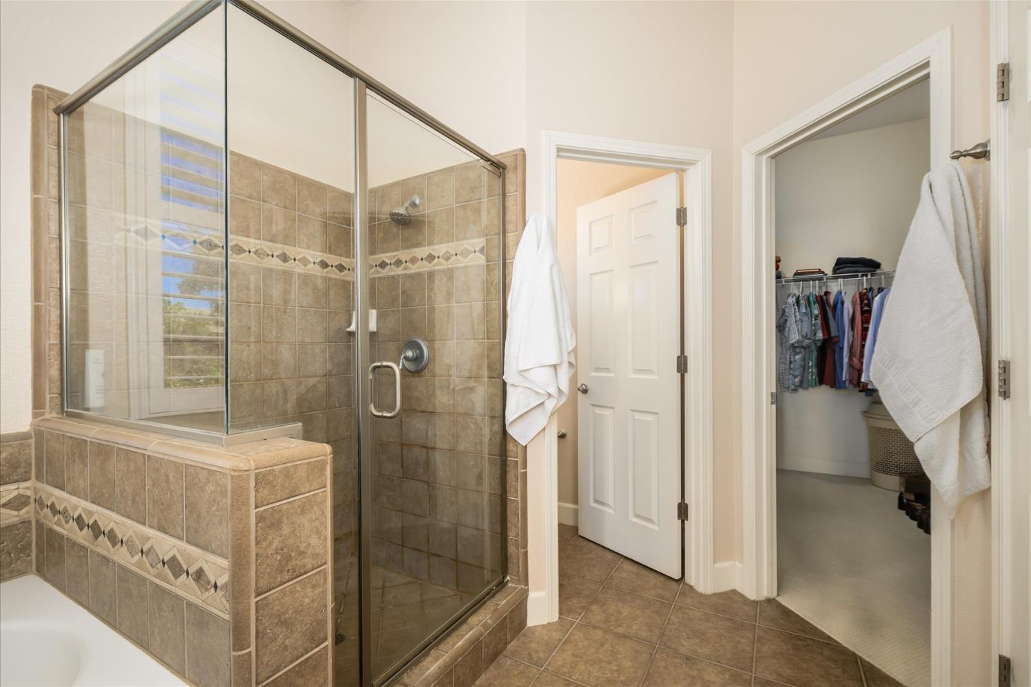 Tiled bathroom with a glass shower, decorative tile accents, and an open doorway to a clothes-filled closet.