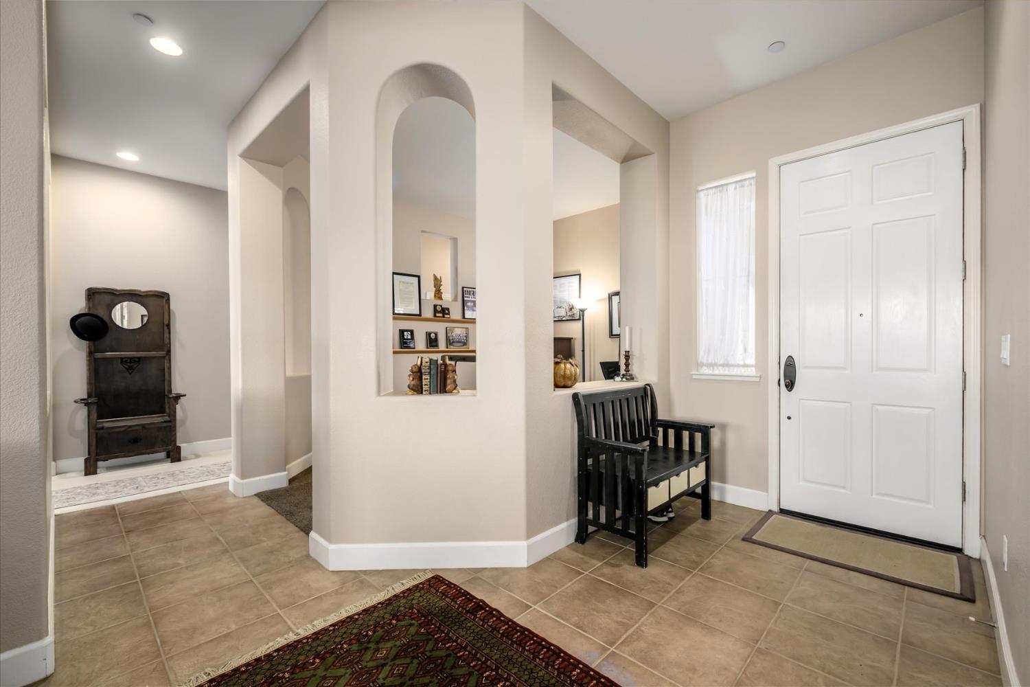 Entry foyer with tiled floors, arched openings, and a black wooden bench beside the front door.