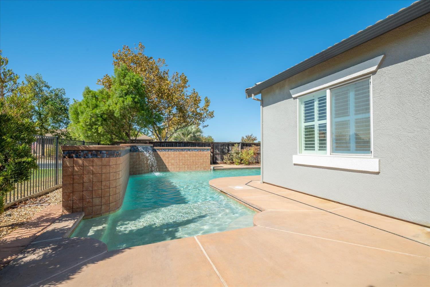Backyard pool with a tiled waterfall beside the home and a broad concrete patio.