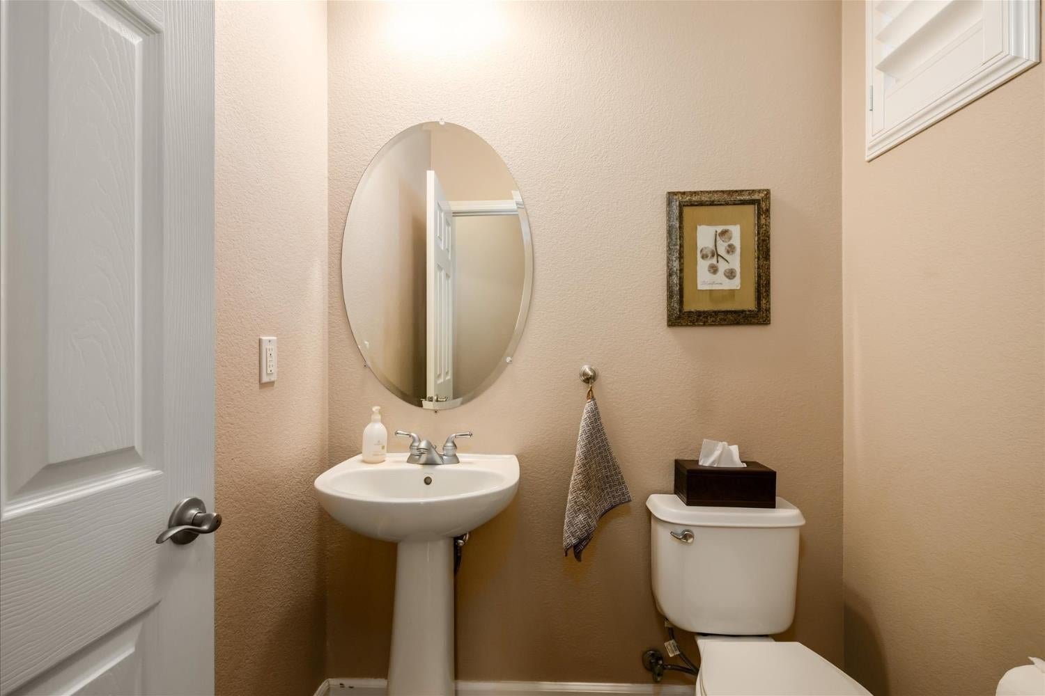 Bathroom with a pedestal sink, oval mirror, and toilet beside an open paneled door.