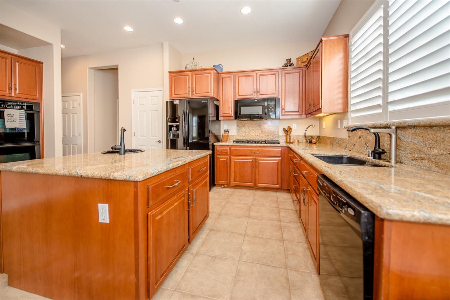 Kitchen with granite counters, reddish wood cabinets, a large island, and white plantation shutters.
