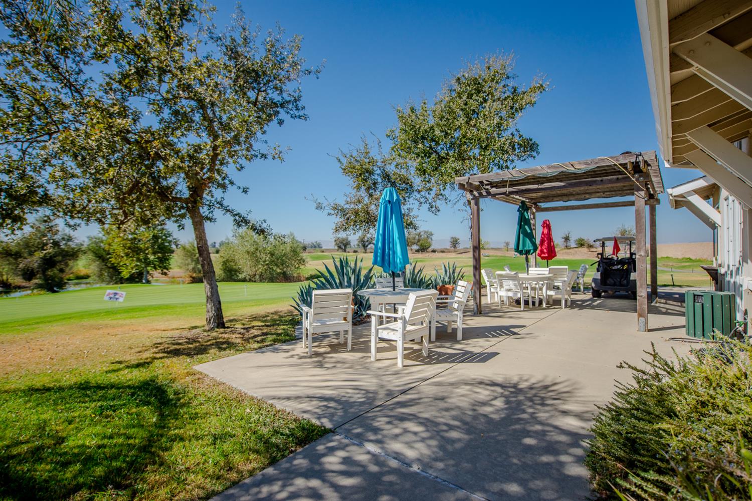Outdoor patio with dining furniture and a wooden pergola overlooking a golf course.