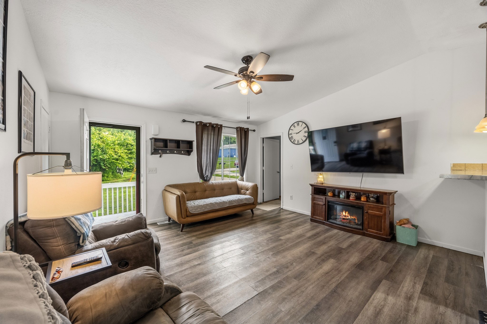Furnished living room with a wall-mounted television, fireplace console, and glass door to a porch.