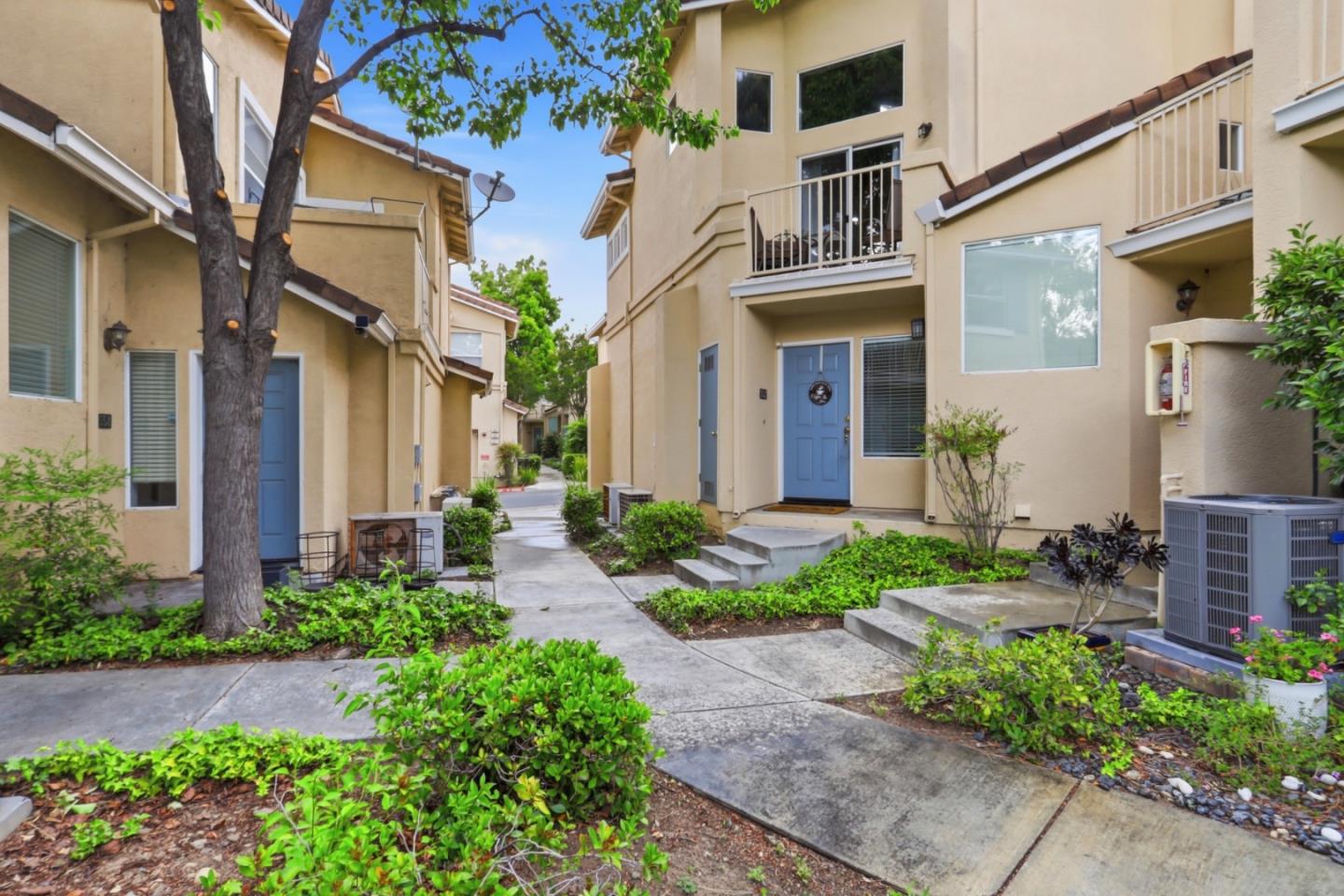 Beige townhomes with blue doors and balconies along a landscaped courtyard walkway.